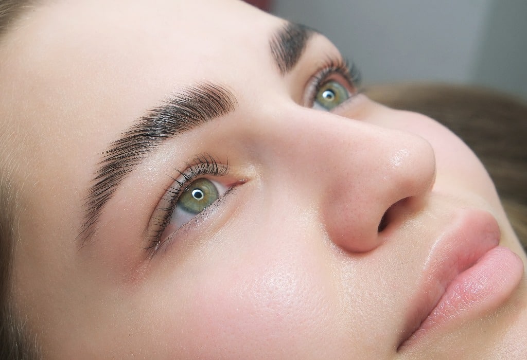 Sable style eyebrows concept. Close up portrait of young sensual model with clean skin, professional make up and beautiful green eyes, laminated eyelashes, tropical background with fern leaves.